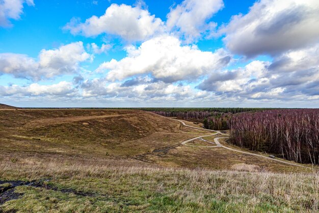 Paisaje panorámico de la llanura del valle con senderos y árboles en el bosque contra el cielo azul con nubes blancas en el horizonte en el fondo Thor Park Parque Nacional Hoge Kempen soleado día de otoño en Genk Bélgica