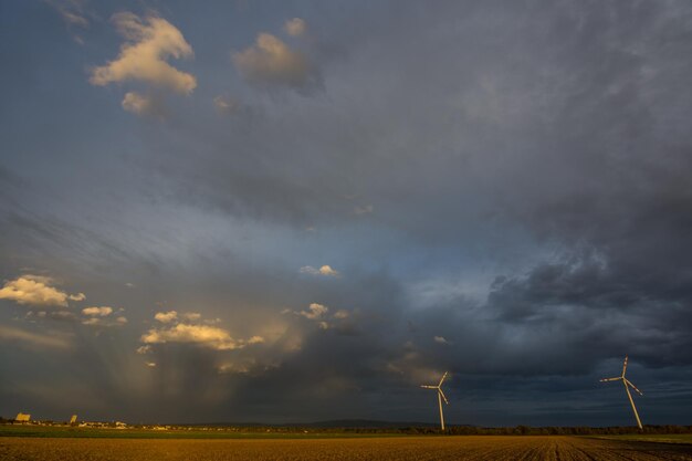 Paisaje plano con casas dos molinos de viento y rayos de sol entre nubes de lluvia