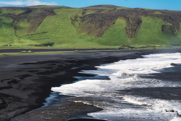 Paisaje de playa de arena negra Reynisfjara con cordillera verde en la costa sur en verano en Islandia