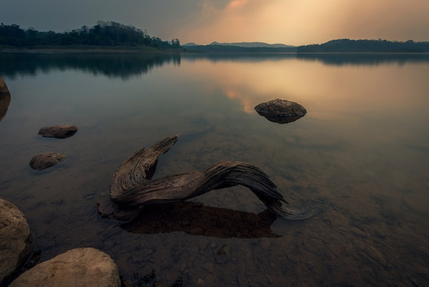 Paisaje de una puesta de sol sobre el agua del lago con madera- Imagen