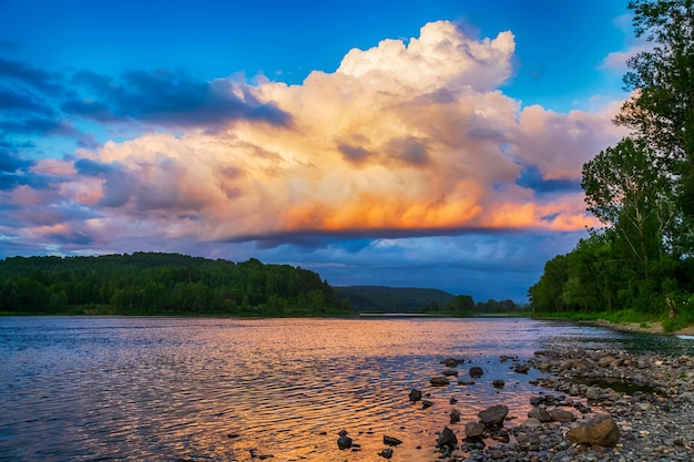 Paisaje de río de verano con cielo azul nublado y puesta de sol