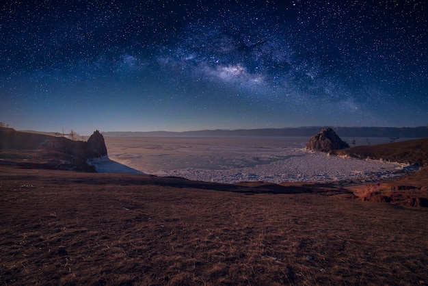 Paisaje de roca Shamanka y vía láctea en el cielo con hielo natural en agua congelada en el lago Baikal, Siberia, Rusia.