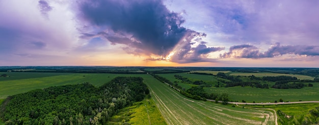 Paisaje rural de puesta de sol de verano con campos verdes y panorama de vista aérea de fondo natural de cielo colorido dramático