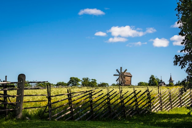 Paisaje rural de verano detrás de una valla de madera, un antiguo molino de viento y una iglesia de madera