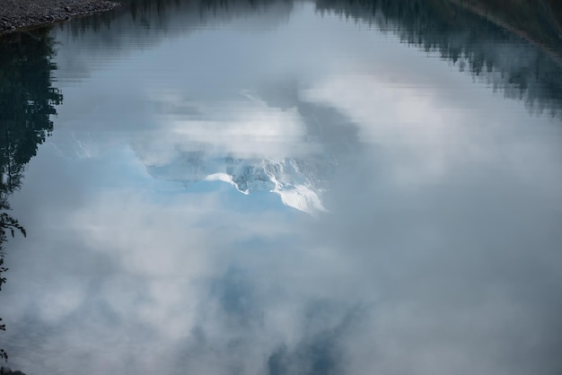 Paisaje tranquilo con reflejo en el lago de montaña del castillo de nieve en las nubes Montañas nevadas en la niebla y árboles coníferos reflejados en el lago alpino Hermoso paisaje con espejo del lago glacial