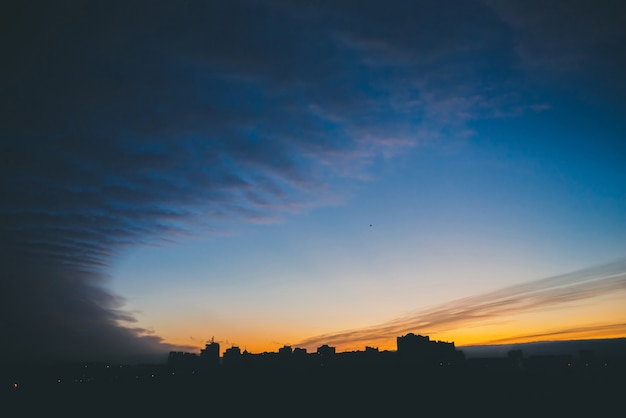 Paisaje urbano con maravilloso amanecer vivo multicolor. Increíble cielo espectacular nube azul sobre siluetas oscuras de techos de construcción de la ciudad.