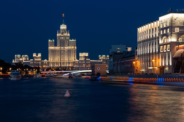 Paisaje urbano nocturno con rascacielos de estilo imperio brillantemente iluminados en la orilla de un río