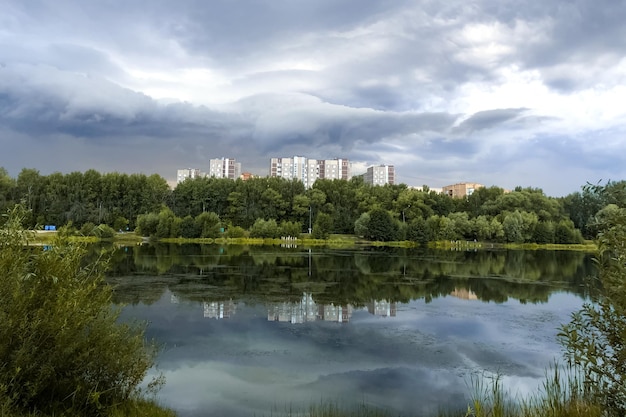 Paisaje de verano con superficie de agua de lago con cielo nublado y edificios de varios pisos reflejados en él