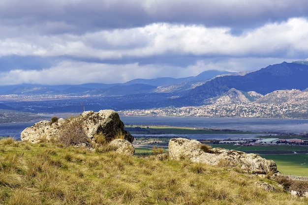 Paisaje verde con grandes rocas, lago y montañas en el fondo y nubes blancas en el cielo azul. Navacerrada Madrid. Europa.