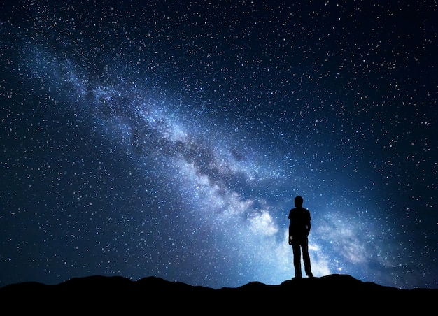 Paisaje con Vía Láctea azul. Cielo nocturno con estrellas y silueta de un hombre feliz en la montaña.