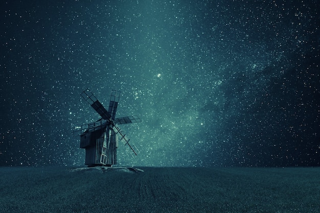 Paisaje vintage de noche con antiguo molino de viento en campo, estrellas brillantes en el cielo, galaxia sin fin. Filtro de película