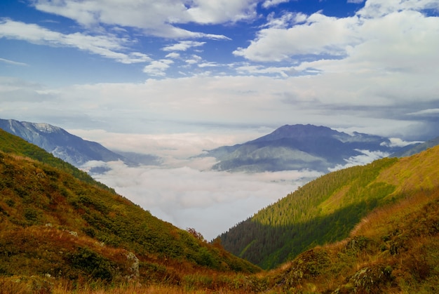 Paisaje: vista desde la cima de la montaña en un día soleado hasta el valle oculto por nubes bajas