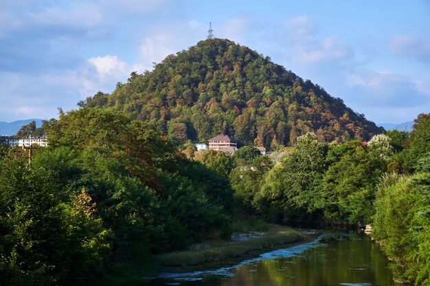 Paisaje en una zona montañosa con una colina, un río y una torre de transmisión de energía en la parte superior