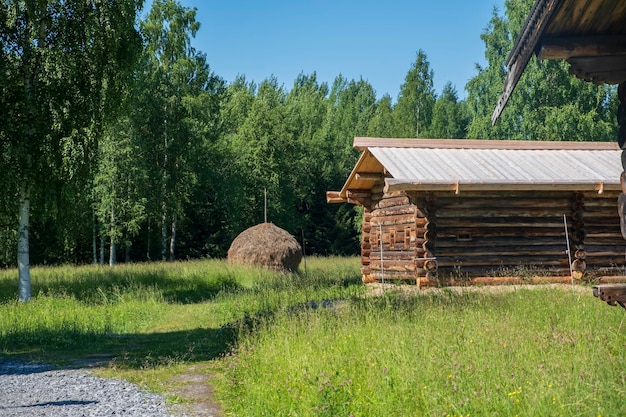 Un pajar en un prado de verano cerca de una casa de madera en el campo