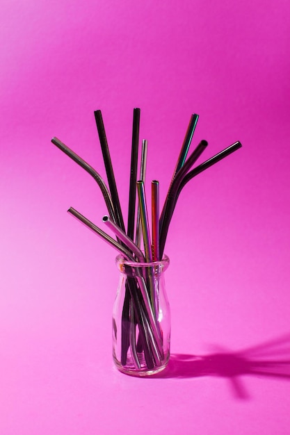 Pajas de beber de aluminio de varias formas y tamaños en un vaso sobre el fondo púrpura