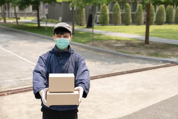 Paketzustellungskonzept Der junge Absender hebt zwei Pakete mit Paketen und steht in der Mitte einer engen Straße, um nach einem Gebäude zu suchen, in dem er diese beiden Pakete fallen lässt.