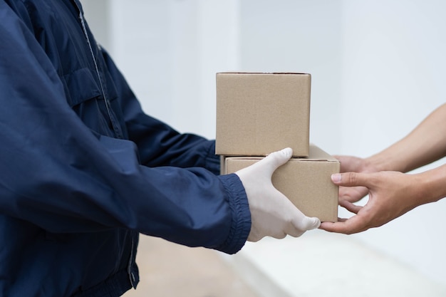 Paketzustellungskonzept Der Postbote in weißen Gummihandschuhen und leichtem dunkelblauem Mantel übergibt seinem Kunden zwei kleine Paketposten.
