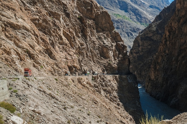 Pakistanische LKWs, die auf gepflasterter Straße entlang dem Berg nahe der Klippe in Karakoram-Landstraße reisen.