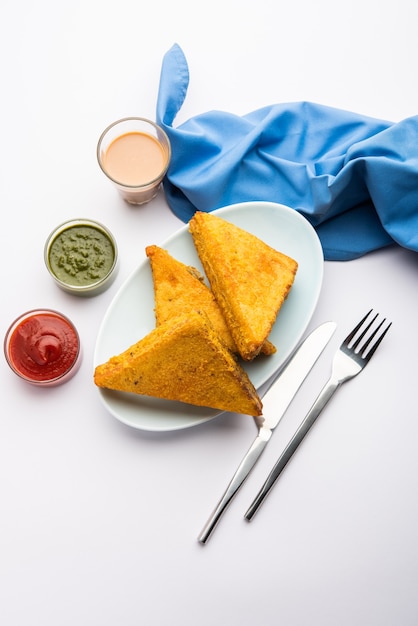 Pakora de pan de sándwich o pakoda en forma de triángulo servido con salsa de tomate, salsa picante verde, refrigerio indio popular a la hora del té