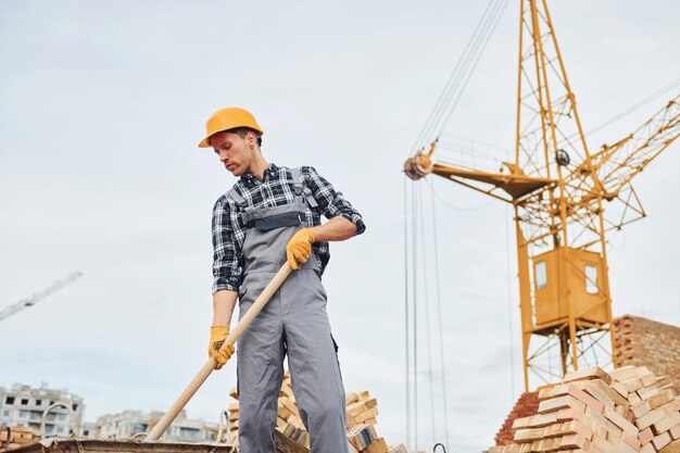 Con pala en las manos Trabajador de la construcción en uniforme y equipo de seguridad tiene trabajo en la construcción