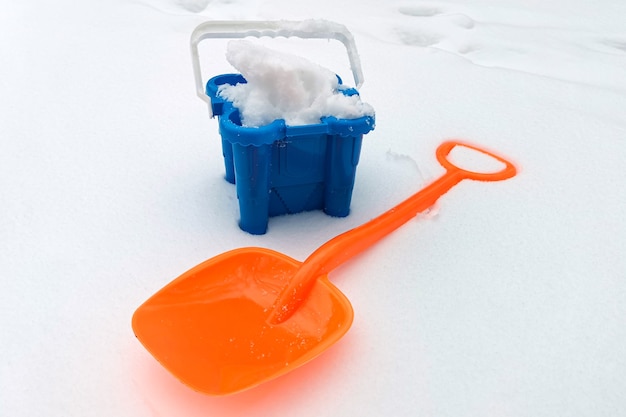 Pala de nieve para niños y balde lleno de nieve en zona nevada. Actividades de invierno al aire libre, accesorios para juegos educativos infantiles con nieve. Actividades de invierno