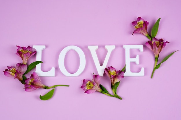 La palabra amor en una pared rosa con flores de alstroemeria. día de San Valentín