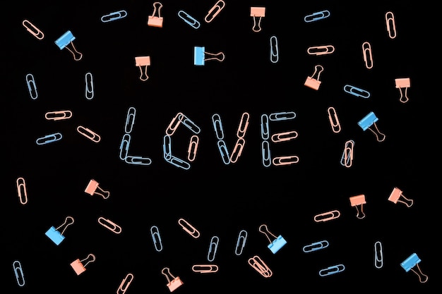 La palabra amor se presenta a partir de clips sobre un fondo negro. Los sujetapapeles son de color rosa y azul. El concepto de San Valentín.