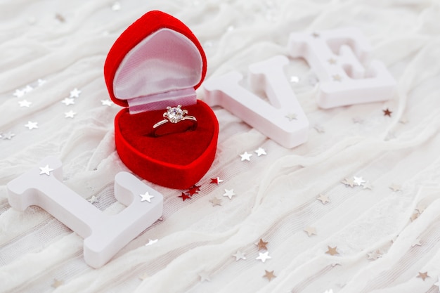 Palabra AMOR sobre fondo de tela blanca con anillo de compromiso en caja de regalo roja.
