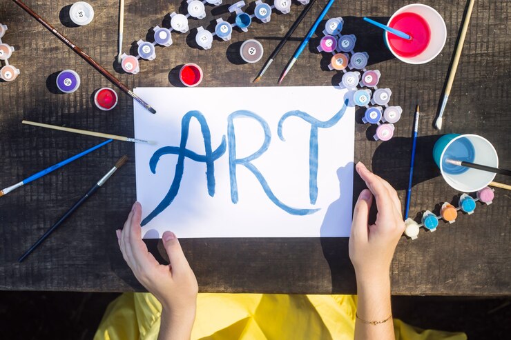 Foto la palabra arte está escrita en pintura azul en una hoja blanca de papel entre los pinceles y pinturas para dibujar. creatividad y concepto de hobby.