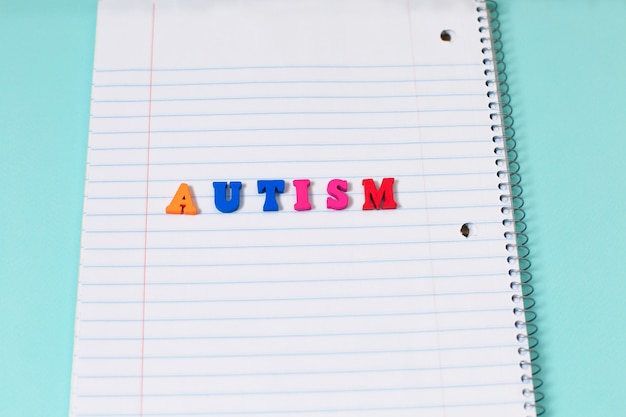 Palabra colorida del autismo de letras de madera del color en la página del cuaderno.