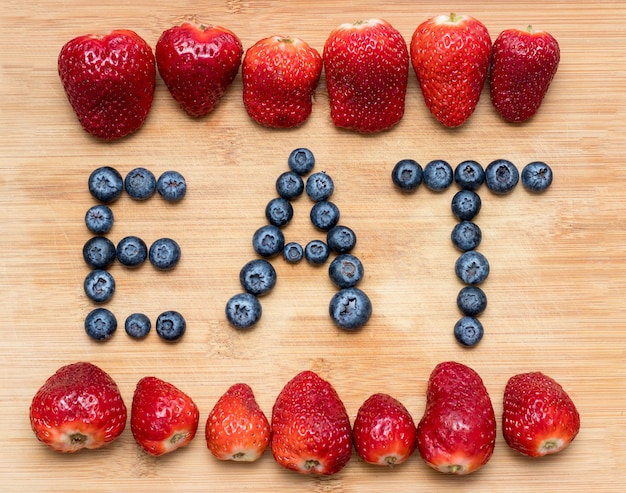 Palabra comer formado con arándanos con fresas en madera.