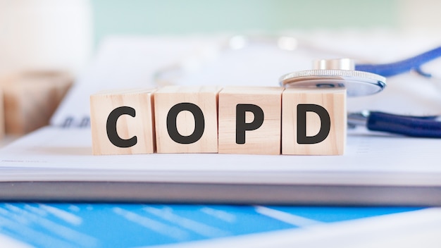 La palabra Copd está escrita en cubos de madera cerca de un estetoscopio sobre una superficie de papel