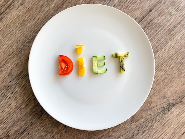 Palabra dieta hecha de verduras en rodajas en un plato blanco sobre fondo de madera