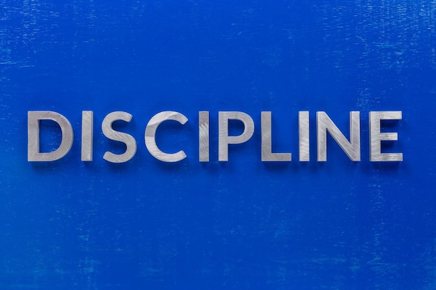 La palabra disciplina colocada con caracteres de metal plateado sobre una tabla de madera pintada de azul en una composición plana central