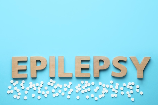 Palabra epilepsia y pastillas sobre fondo azul claro espacio plano para texto