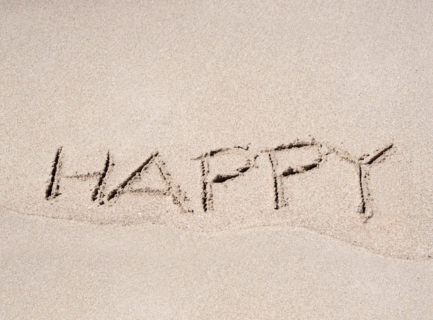 Palabra feliz dibujado en la arena de la playa
