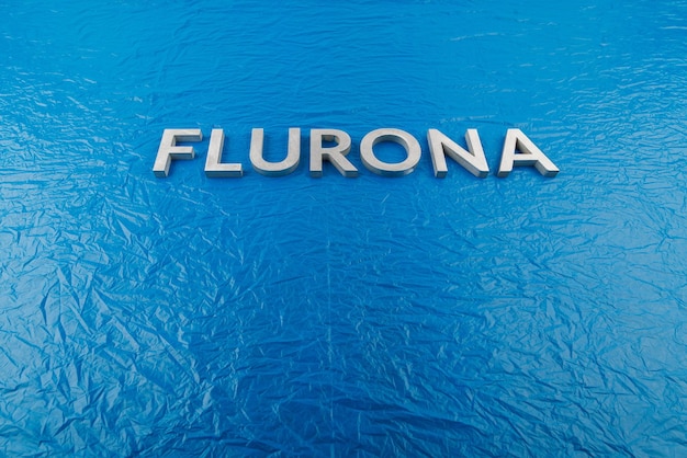 La palabra flurona colocada con letras de metal plateado sobre fondo de película de plástico azul arrugado