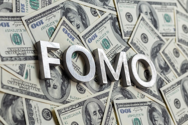 Foto la palabra fomo se colocó con letras de aluminio en el fondo de los billetes en dólares estadounidenses con enfoque selectivo