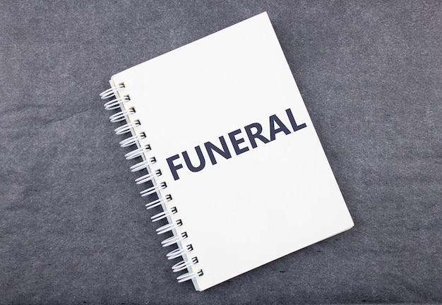 La palabra FUNERAL en un cuaderno sobre un fondo negro oscuro El concepto de organizar un funeral