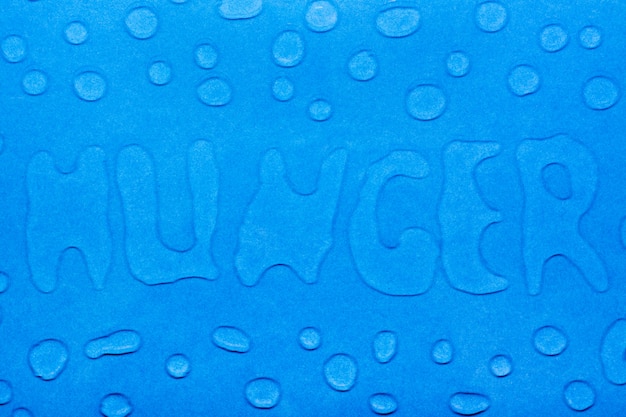 La palabra "hambre" se escribe con gotas de agua y gotas de agua sobre una superficie lisa azul.