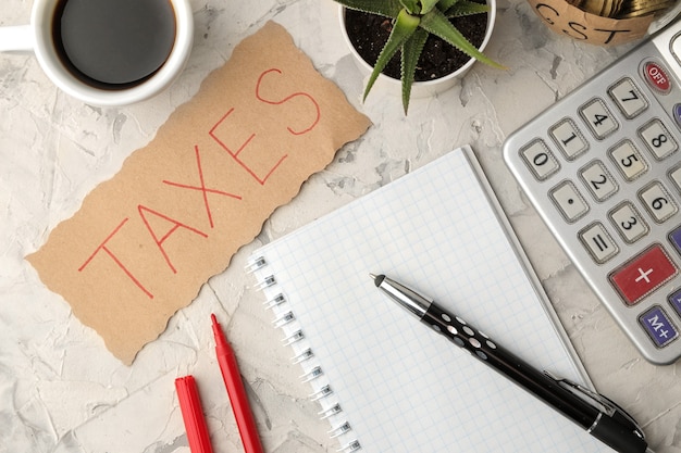 La palabra impuestos en una hoja de papel en un cuaderno con café y bolígrafo sobre un fondo de hormigón claro. vista desde arriba