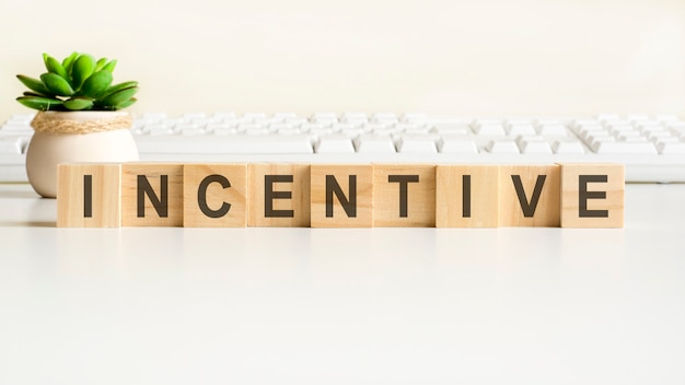 Palabra de incentivo hecha con bloques de madera. Conceptos de vista frontal, planta verde en un florero y teclado blanco sobre fondo