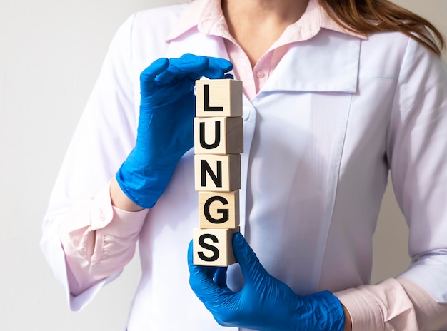 Palabra de LUNGS sobre bloques de cubos en las manos con guantes médicos de una doctora