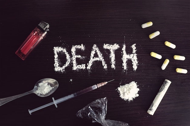 La palabra muerte escrita en cocaína sobre una mesa negra rodeada de diversas drogas duras. El concepto de adicción.