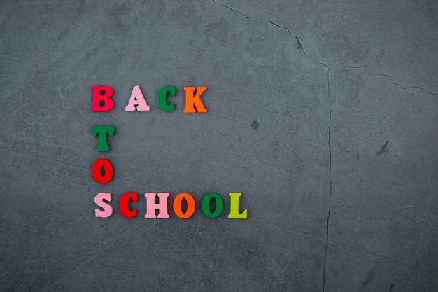 La palabra multicolor de regreso a la escuela está hecha de letras de madera en una pared enlucida gris.