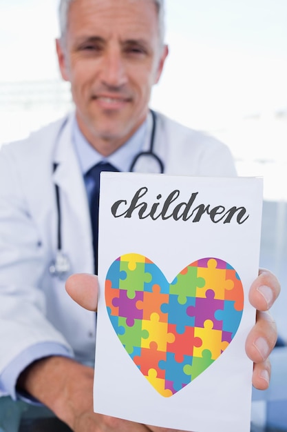 La palabra niños y el retrato de un médico que muestra una hoja de prescripción en blanco contra el corazón de la conciencia del autismo