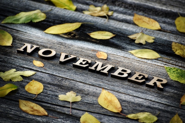 Palabra noviembre Letras de madera marco de hojas amarillas fondo de madera