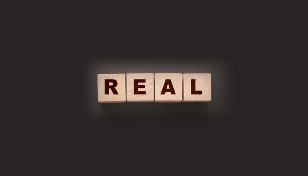 Palabra real en cubos de madera en negro Concepto de negocio inmobiliario Falso y real