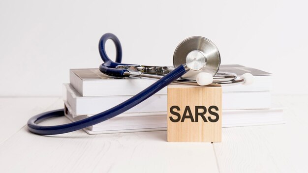 La palabra SARS está escrita en un cubo de madera cerca de un estetoscopio en un concepto médico de fondo blanco