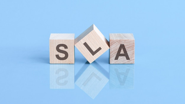 La palabra SLA está formada por cubos de madera sobre la mesa azul, concepto de negocio. SLA abreviatura de Acuerdo de nivel de servicio